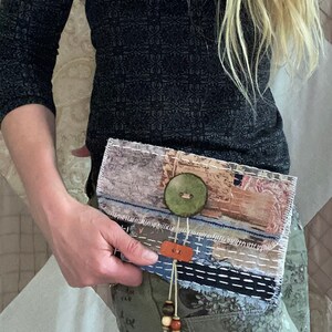 May include: A small, multi-colored fabric clutch with a large green button and a brown leather strap with wooden beads. The clutch is made of various fabrics and has a patchwork design.