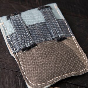 May include: A small, gray and blue fabric pouch with a zipper closure and a decorative tassel. The pouch is made of a patchwork of different fabrics and has a rustic, handmade look.