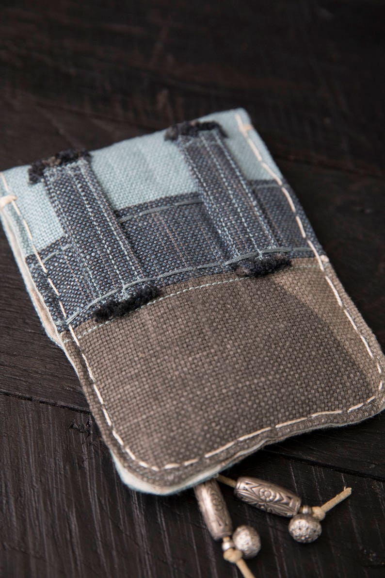 May include: A small, gray and blue fabric pouch with a zipper closure and a decorative tassel. The pouch is made of a patchwork of different fabrics and has a rustic, handmade look.