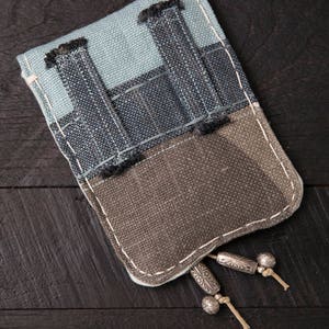 May include: A small, rectangular pouch made of blue and brown fabric with a zipper closure and silver tassels. The pouch is made of a patchwork of different fabrics.