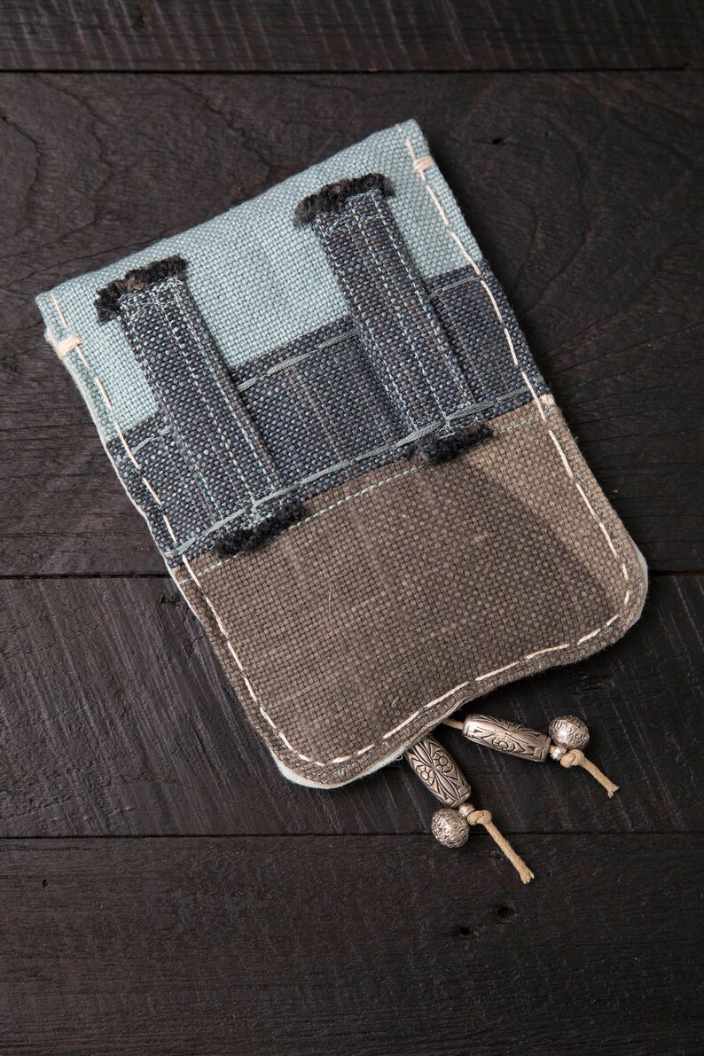 May include: A small, rectangular pouch made of blue and brown fabric with a zipper closure and silver tassels. The pouch is made of a patchwork of different fabrics.
