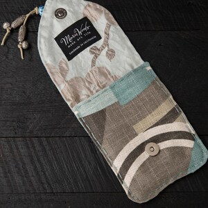 May include: A small, light blue and brown fabric pouch with a snap closure. The pouch has a floral pattern on one side and a geometric pattern on the other. The pouch is handmade in California by Maria Woods.