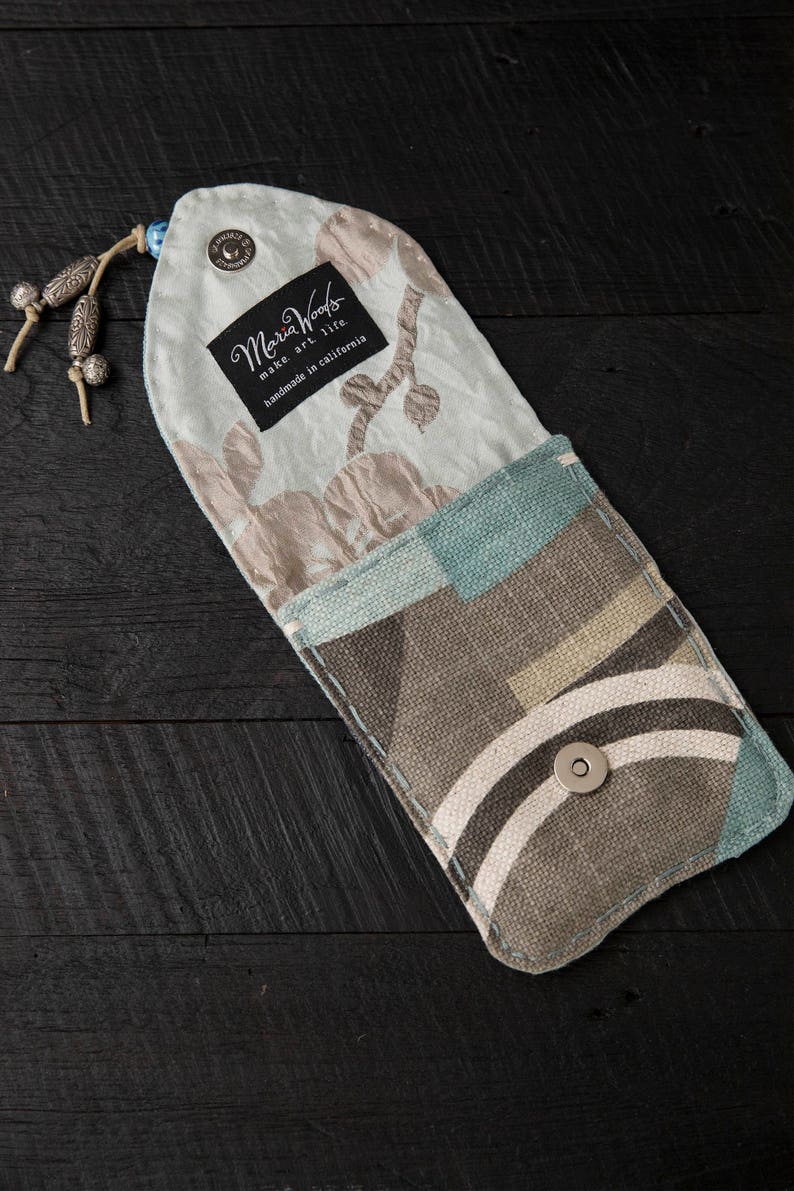 May include: A small, light blue and brown fabric pouch with a snap closure. The pouch has a floral pattern on one side and a geometric pattern on the other. The pouch is handmade in California by Maria Woods.