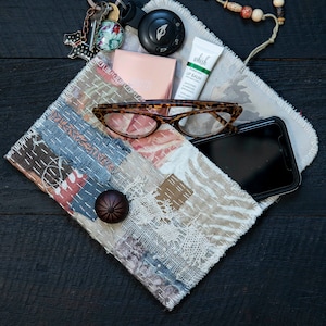 May include: A patchwork fabric pouch with a frayed edge, containing a pair of glasses, a cell phone, a lip balm tube, a small compact, a key chain with a car key, and a beaded string.