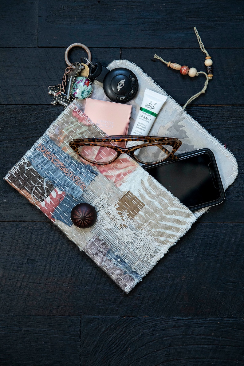 May include: A patchwork fabric pouch with a frayed edge, containing a pair of glasses, a cell phone, a lip balm tube, a small compact, a key chain with a car key, and a beaded string.