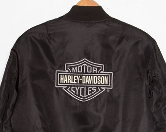 May include: Black bomber jacket with a Harley-Davidson logo on the back. The logo is embroidered in silver thread.