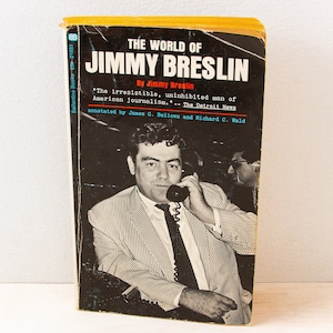 以下が含まれることがあります： ジミー・ブレズリンの「ジミー・ブレズリンの世界」というタイトルの黄色と黒のペーパーバック。本の表紙には、電話をしている男性の白黒写真が掲載されている。表紙のテキストには、「アメリカのジャーナリズムの、魅力的で、抑制のない男。」- デトロイト・ニュース。ジェームズ・G・ベローズとリチャード・C・ワルドによる注釈。