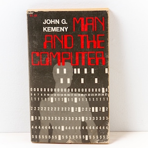 May include: A vintage paperback book titled "Man and the Computer" by John G. Kemeny. The cover features a black and white silhouette of a person with a grid of numbers in the background.