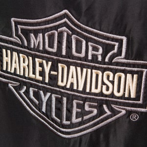 May include: A black embroidered patch with the Harley-Davidson logo in white and gray. The logo features the words "Motor", "Harley-Davidson", and "Cycles" in a shield shape.