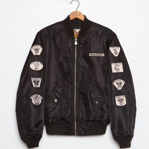 May include: Black bomber jacket with multiple Harley Davidson patches on the sleeves. The patches feature different motorcycle engine designs and dates.