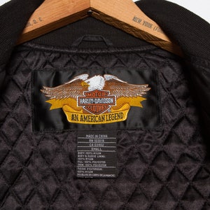 May include: Black Harley-Davidson jacket with a quilted lining and a satin label that reads "Motor Harley-Davidson Clothes An American Legend". The label has an embroidered eagle with a yellow banner.