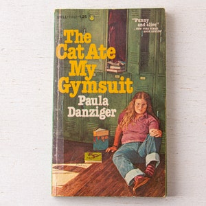 May include: A book cover with a yellow title "The Cat Ate My Gymsuit" by Paula Danziger. The cover features a young girl sitting on the floor in front of a row of green lockers. The book is a classic children's novel.