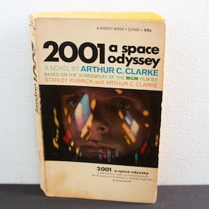 May include: Vintage paperback book titled "2001: A Space Odyssey" by Arthur C. Clarke. The cover features a portrait of a person with colorful light reflections. The book is a Signet Book.