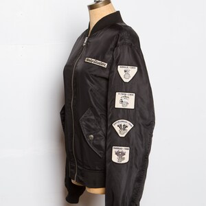 May include: Black bomber jacket with a Harley Davidson logo and patches on the sleeve. The patches feature the text "Single - 1903", "V-Twin - 1909", "Knucklehead - 1936", and "Panhead - 1940".