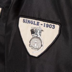 May include: A black patch with white stitching and the text "SINGLE - 1903" in blue. The patch features a black and white illustration of a motorcycle engine.