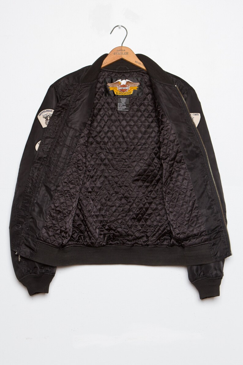 May include: Black bomber jacket with a quilted lining and Harley Davidson patches on the sleeves. The patches feature the Harley Davidson logo and the words "An American Legend".