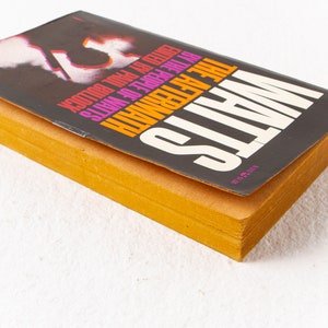May include: A paperback book titled "The Aftermath" by the author "Watts" with the text "VICTOR GOLLANCZ LTD" on the bottom right corner of the cover. The cover is black with pink, orange, and yellow text.
