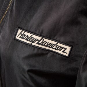 May include: Black jacket with a Harley Davidson logo patch on the left chest and a smaller patch on the right sleeve.