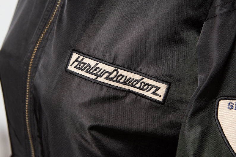 May include: Black jacket with a Harley Davidson logo patch on the left chest and a smaller patch on the right sleeve.