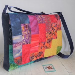 May include: A patchwork messenger bag with a blue strap. The bag is made of colourful fabric with a variety of patterns, including floral, geometric, and abstract designs.