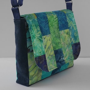 May include: A blue and green patchwork fabric crossbody bag with a navy blue strap and a flap closure.