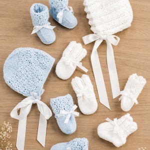 May include: A collection of baby accessories including two light blue bonnets with white ribbon ties, two pairs of light blue knit booties with white ribbons, and three pairs of white knit mittens with white ribbon bows, all featuring a textured pattern.