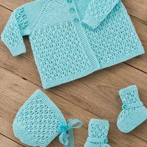 May include: A light blue knitted baby set consisting of a long-sleeved cardigan with three buttons, a bonnet with a matching ribbon tie, and a pair of booties. Each piece features a delicate openwork lace pattern combined with solid knit sections.