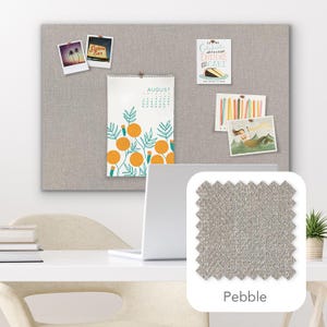 Pu&ograve; includere: Una bacheca in tessuto grigio chiaro con diversi elementi decorativi appuntati, tra cui un calendario, cartoline e foto. Un campione di tessuto etichettato "Pebble" &egrave; mostrato in basso a destra. Un laptop e una scrivania sono in primo piano.