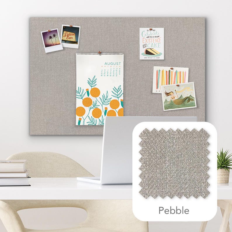 Pu&ograve; includere: Una bacheca in tessuto grigio chiaro con diversi elementi decorativi appuntati, tra cui un calendario, cartoline e foto. Un campione di tessuto etichettato "Pebble" &egrave; mostrato in basso a destra. Un laptop e una scrivania sono in primo piano.
