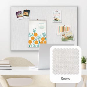 Pu&ograve; includere: Una bacheca in tessuto bianco con vari elementi decorativi appuntati, tra cui un calendario di agosto con illustrazioni di arance e diverse piccole immagini. Un campione di tessuto &egrave; etichettato "Snow".