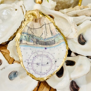 May include: Gold-trimmed oyster shell ornament with a nautical map and compass design. The map shows Ocean Isle Beach, North Carolina.