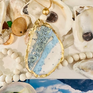 May include: A gold-painted oyster shell ornament with a map of a coastal area inside. The map shows numbered waterways and the text "de R."