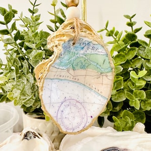 May include: A gold-painted oyster shell ornament with a nautical map of Cumberland Island, Georgia. The map features a compass rose and the text "Cumberland Island".