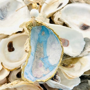 May include: A gold-rimmed oyster shell with a blue and white map design inside. The shell is surrounded by other oyster shells.
