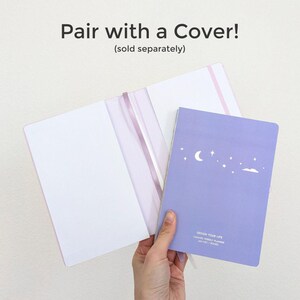 May include: A lavender weekly planner with a crescent moon and star design, held next to a pink notebook cover. The text "Pair with a Cover!" is displayed above the notebooks.