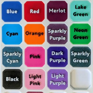 May include: A white PETG color options chart featuring a grid of square samples with rounded corners. Each sample is labeled with text including Blue, Red, Merlot, Lake Green, Cyan, Orange, Sparkly Purple, Neon Green, Sparkly Cyan, Pink, Dark Purple, Sparkly Green, Black, Light Pink, Light Purple, and Sparkly Pink.