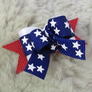 May include: A red, white, and blue bow with white stars on a blue background. The bow is tied with a red star-shaped clip.