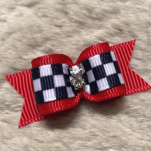 May include: A red and white checkered bow with a small, sparkling embellishment in the center. The bow has red ribbon accents and is likely a hair accessory or decorative item.
