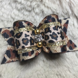 May include: A small leopard print bow with gold trim and a clear rhinestone in the center.