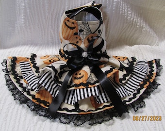Puede incluir: Vestido para perro con temática de Halloween, con estampado de calabazas y telarañas. La falda es a rayas blancas y negras, con ribete de encaje negro. Un gran lazo negro adorna el vestido.