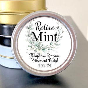 May include: A stack of small, round tins in gold, black, and white. One tin is in focus, displaying the text "Retire Mint" with floral accents, and the text "Theophous Reagans Retirement Party! 3-23-24".