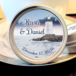 May include: A silver tin with a white and blue label featuring a lighthouse, ocean waves, and the text "Kristi & Daniel December 17, 2016". The lid of the tin has the text "Thank you for sharing this special day with us!"