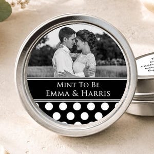 May include: Two round silver metal tins with custom labels. The front tin features a black and white photograph of a couple, the text "MINT TO BE EMMA & HARRIS," and a white polka dot pattern. The side tin has text about sharing love.