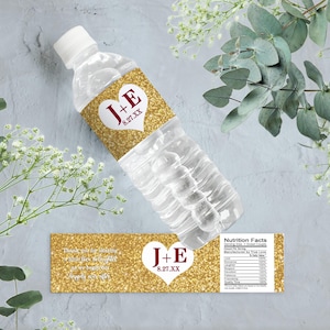 Op de afbeelding: Gouden glitter bruiloft waterfles label met een wit hart en de tekst "J+E 8.27.XX". Het label bevat ook de tekst "Bedankt dat je met ons feestviert!" en een voedingswaardelabel.