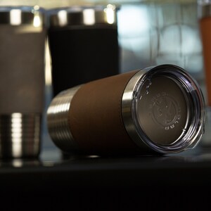 May include: A brown leather-wrapped stainless steel tumbler with a clear lid. The lid has a silver logo that says "The Good Life".