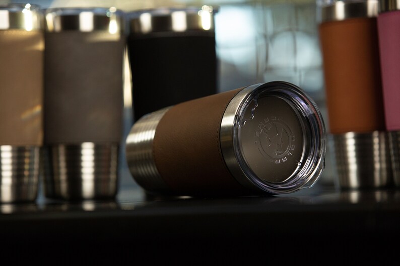 May include: A brown leather-wrapped stainless steel tumbler with a clear lid. The lid has a silver logo that says "The Good Life".