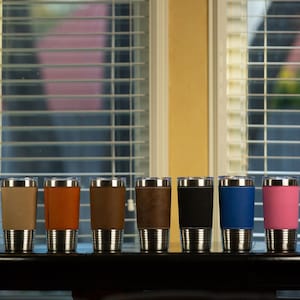 May include: Ten stainless steel travel mugs with different colored faux leather wraps. The colors are gray, beige, orange, brown, dark brown, black, blue, pink, and light blue.