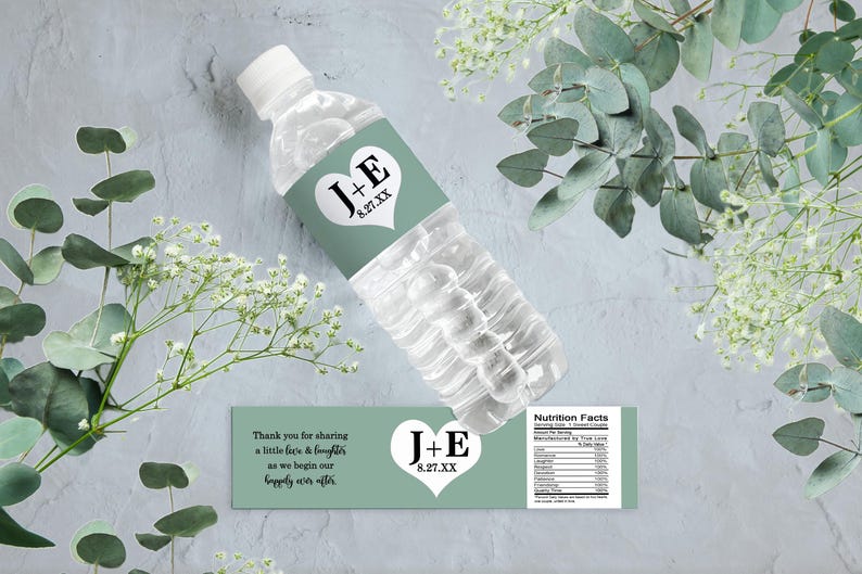 Op de afbeelding: Een groen en wit bruiloftwaterfleslabel met de tekst "J+E 8.27.XX" en een hartontwerp. Het label bevat ook de tekst "Bedankt voor het delen van een beetje liefde en gelach terwijl we beginnen aan ons geluk voor altijd."