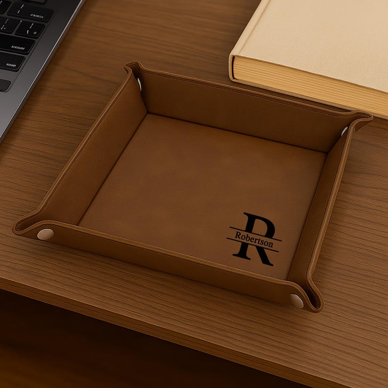 Pode incluir: Uma bandeja de couro castanho com um monograma personalizado e o nome "Robertson" em preto. A bandeja &eacute; quadrada com cantos arredondados e fechos de press&atilde;o. Um laptop e um livro est&atilde;o no fundo.
