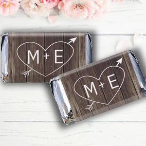 May include: Two chocolate bar wrappers with a rustic woodgrain background. Each wrapper features a white heart with the initials "M+E" and an arrow.